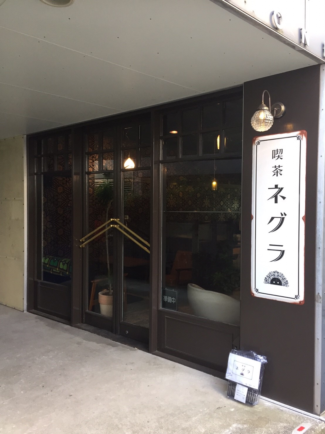 茶色の外壁にガラス扉と「喫茶ネグラ」縦看板、ガラス越しに店内の照明とソファーが見える昼間の外観