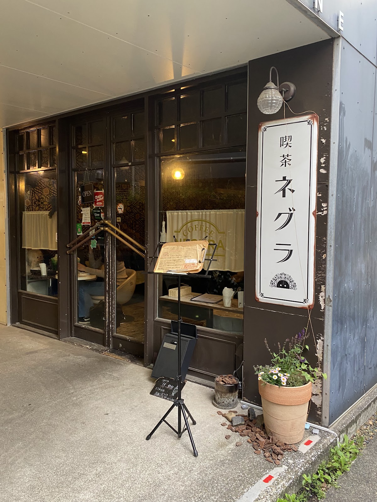 外壁に蔦が茂る路地にA型看板とメニューボードが立つ昼間の外観